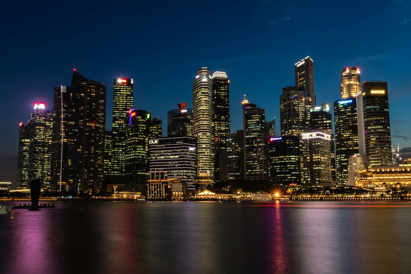 Singapore's central business district lit at night across Marina Bay, bank towers reflected in still water